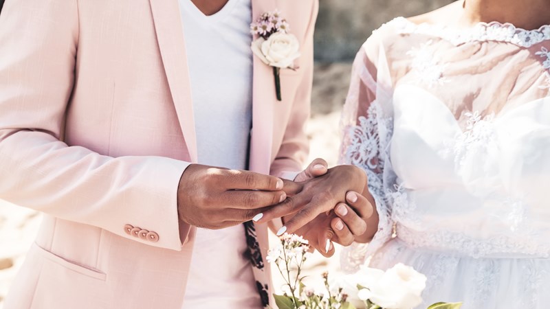 groom-in-pink-jacket-wears-ring-on-the-finger-of-the-bride-on-the-beach.jpg