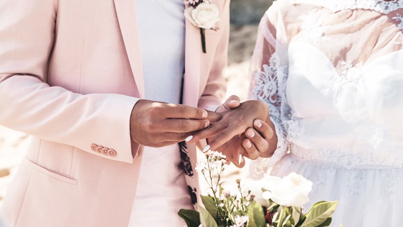 groom-in-pink-jacket-wears-ring-on-the-finger-of-the-bride-on-the-beach.jpg